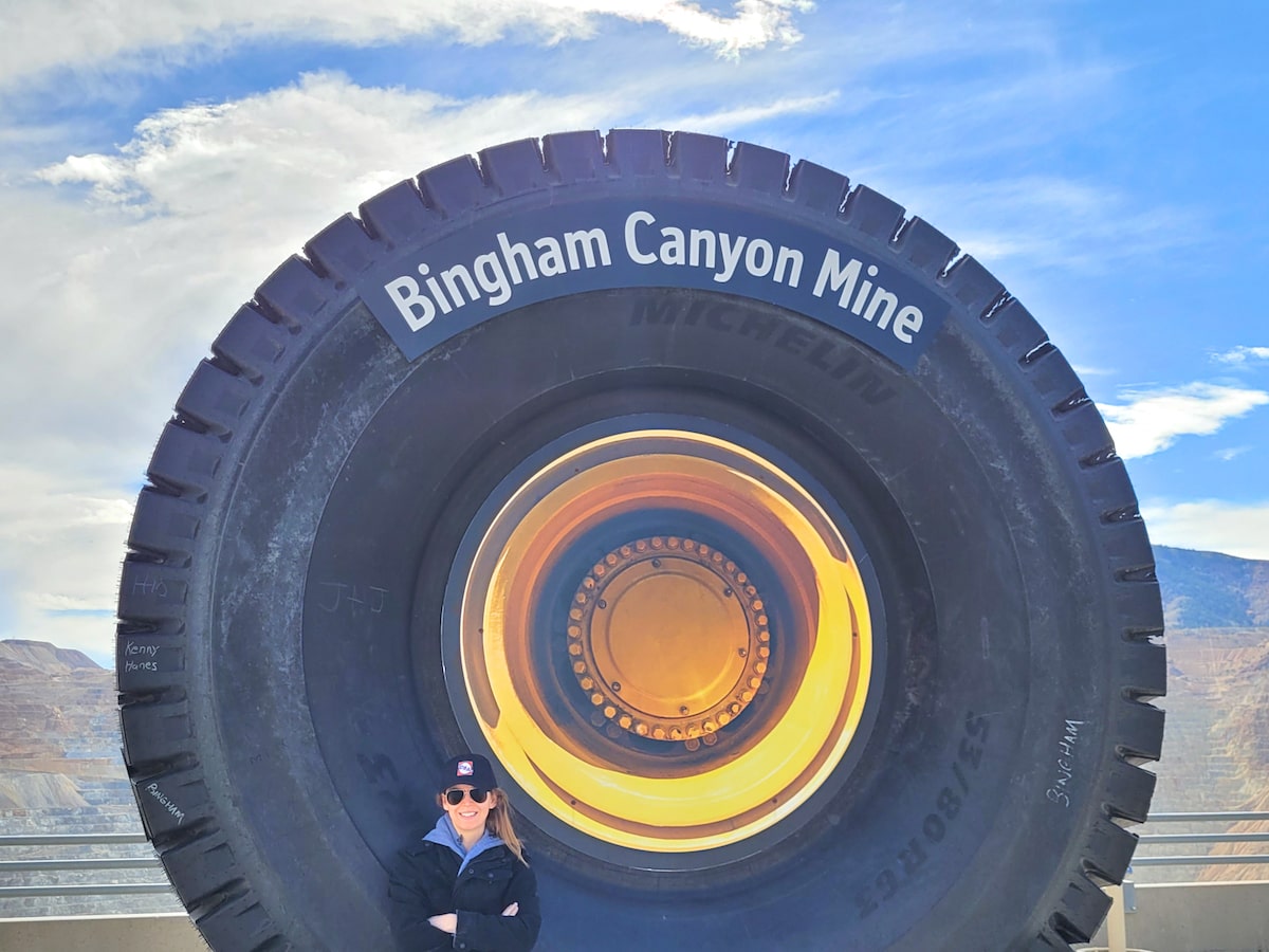 Woman standing in front of big wheel with the sign Bingham Canyon Mine