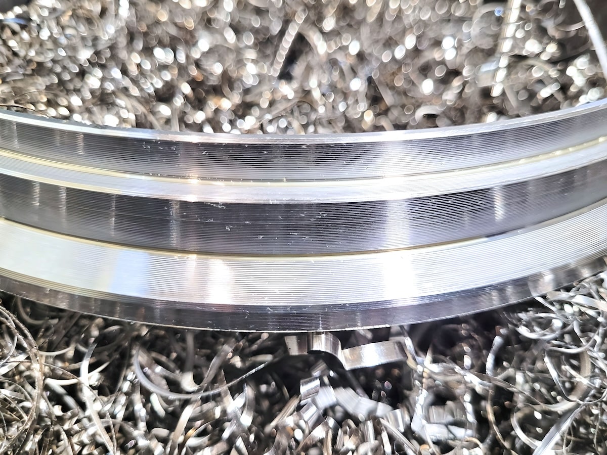 Close-up view of a precision-machined V-band exhaust flange surrounded by metallic shavings