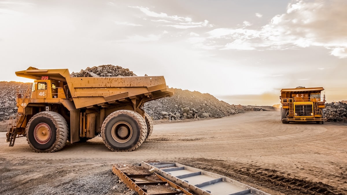 Two Large Mining Haul Trucks Transporting Ore Across A Platinum Mining Site At Sunset, Emphasizing Scale And The Importance Of Mining Truck Safety On-Site.