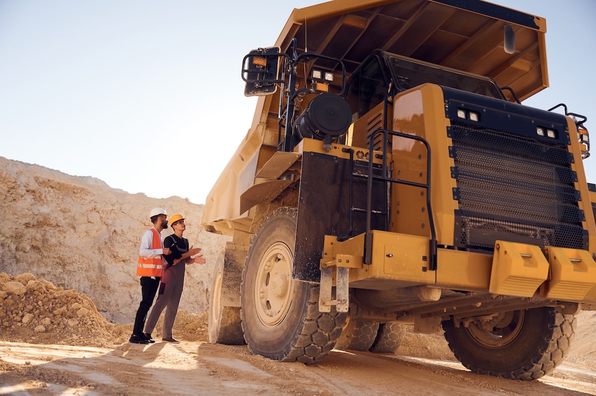 Two Engineers In Safety Gear Inspecting A Massive Haul Truck In A Mining Area, Focusing On Inspection Routines And Mining Truck Safety Practices.